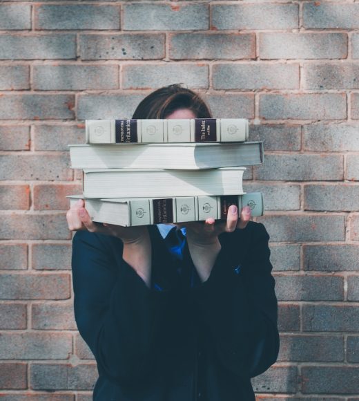 person holding pile of books near face